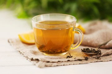 Glass cup of green tea with sliced lemon on wooden table with sackcloth closeup