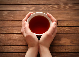 Female hands holding cup of tea on wooden background
