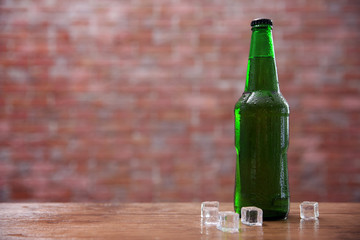 Green glass bottle of beer and  and ice cubes on brick wall background