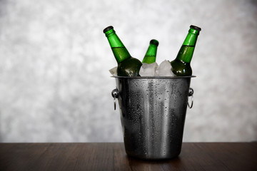Green glass bottles of beer in ice-pail on grey background