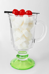 Irish coffee glass with lump sugar and cocktail cherries on grey background
