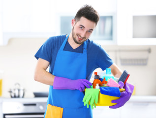 Man holding plastic basin with brushes, gloves and detergents in the kitchen