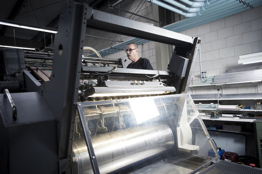 Worker operating printing machine in print workshop