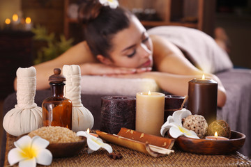 Beautiful young girl with towel lying on massage table and aromatic candles with salt in spa salon