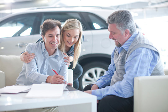 Car salesman and couple signing contract in car showroom