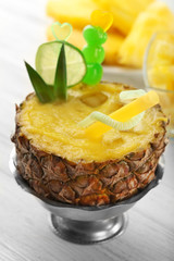 Delicious cocktail in half of pineapple on wooden table closeup