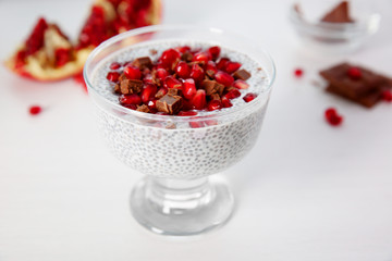 Chia seeds pudding with pomegranate grains and chocolate chips in glass saucer on white background