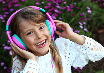  Happy smiling girl with long blond hair, lace clothes listening to music on headphones on a purple blossom flowers background