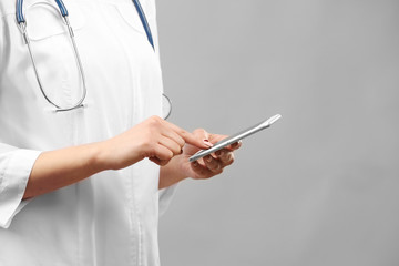 Young female doctor using mobile phone on grey background