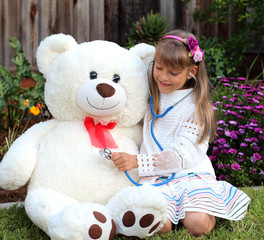  Smiling  girl plays a doctor game with a huge toy white bear