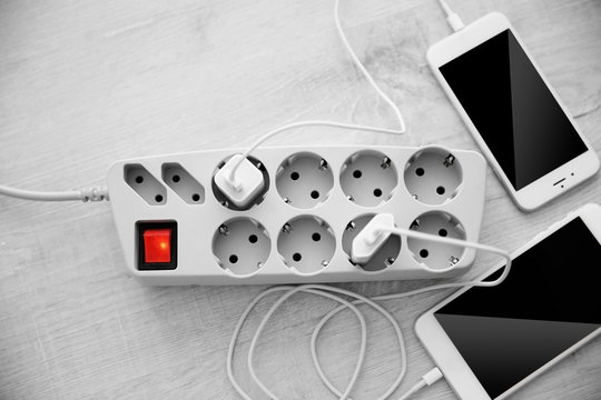 Mobile Phones Charging Into Power Cord On Wooden Floor, Top View