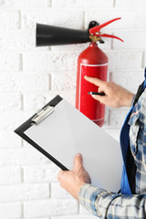 Man inspecting the fire extinguisher against white brick wall background