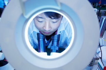 Worker at small parts manufacturing factory in China looking through microscope