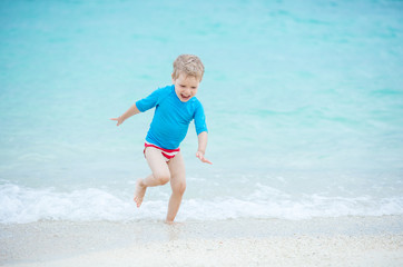 Happy little boy running in breaking waves on beach