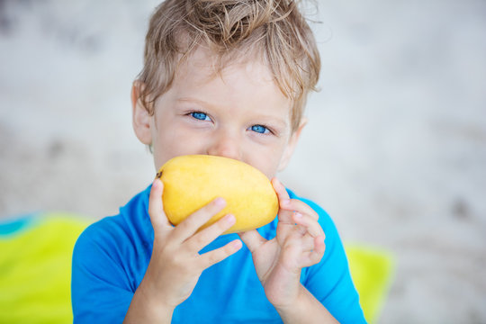 Cute Little Boy With Mango Fruit On Beach 