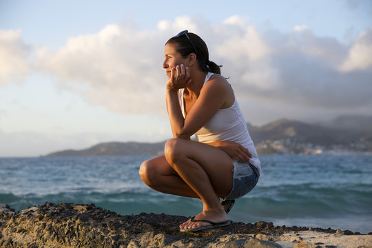 Mid adult woman crouching and gazing at caribbean sea from pier,  Spice Island beach resort, Grenada,
