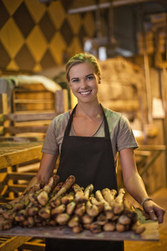 Portrait of young female baker carrying a tray of breadsticks