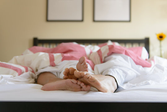 Surface level image of young couple in bed, feet out of duvet
