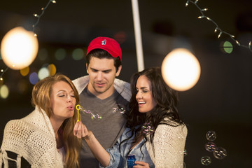 Young adult friends fooling around blowing bubbles at rooftop party