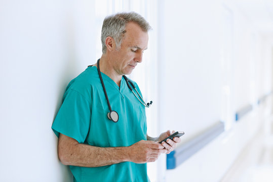Surgeon standing in corridor looking at smartphone