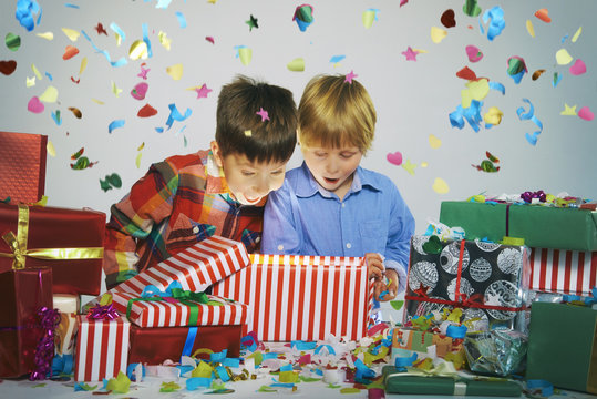 Two brothers open mouthed on unwrapping glowing christmas gift box with exploding confetti