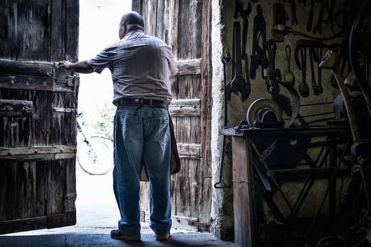 Rear view of senior male blacksmith in opening doors of traditional barn, Cagliari, Sardinia, Italy