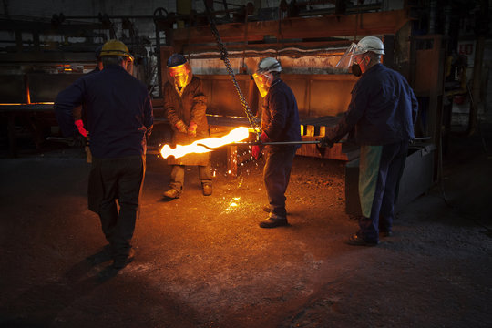 Men hold red hot steel billet 
