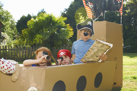 Two brothers and sister playing with homemade pirate ship in garden