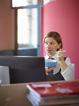 Office worker eating breakfast cereal at desk