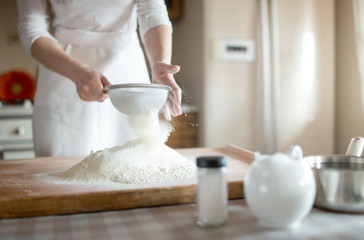 Fototapeta na wymiar young woman sifting flour into bowl at the kitchen