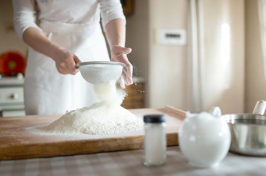 young woman sifting flour into bowl at the kitchen