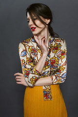 Beautiful young brunette with a distinctive red lipstick captured in studio on grey background. Wears yellow blouse with prints and long skirt.