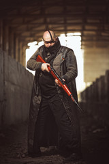 Fototapeta na wymiar Portrait of big brutal man with rifle in leather coat as Mad Max style at abandoned building