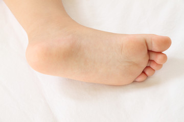 Foot of asian baby on white bedcovers.
