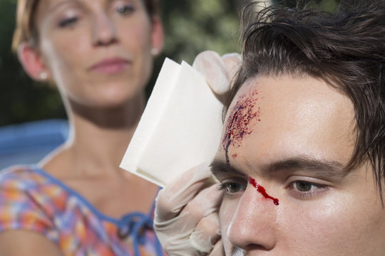 Woman cleaning young man with bleeding forehead