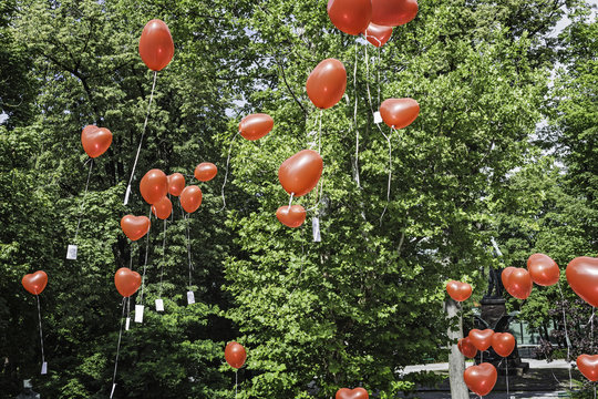 Red heart shaped balloons floating upward from park - Powered by Adobe