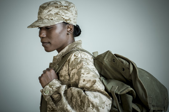 Side view studio portrait of female soldier with rucksack looking down