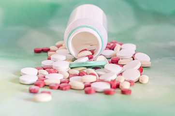 Red, white, yellow drugs pills with white open plastic bottle, powder, bunch, medical, homeopathic, green background, close up