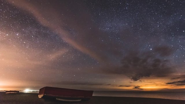 Astro Time Lapse - Lone boat on a beach stars move across the sky and moon rises