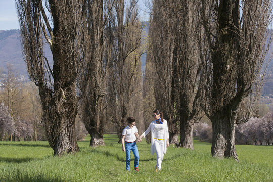 Twelve year old boy and mature mother strolling along tree lined field