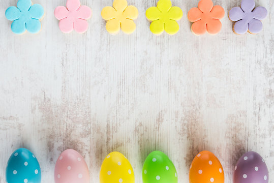 Colorful easter eggs and homemade fondant covered flower cookies on a white wood background