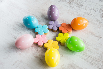 Colorful easter eggs and homemade fondant covered flower cookies on a white wood background