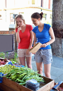 Two young women looking at vegetables at market stall