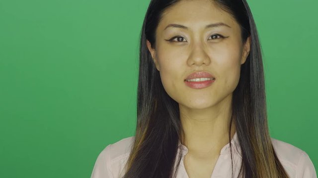 Beautiful Asian woman smiling, on a green screen studio background 