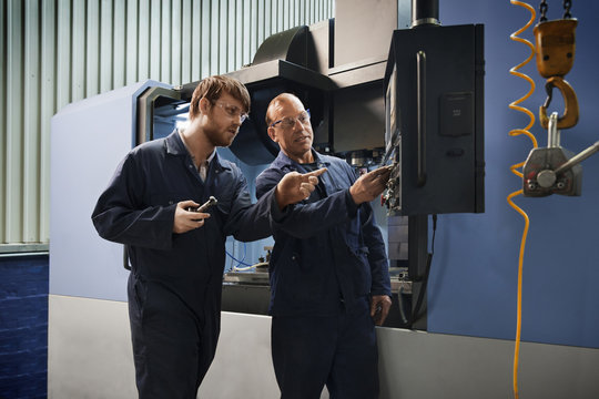 An experienced worker explains the workings of a CNC machine to an apprentice