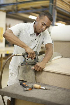 Upholsterer attaching textile to frame using staple gun