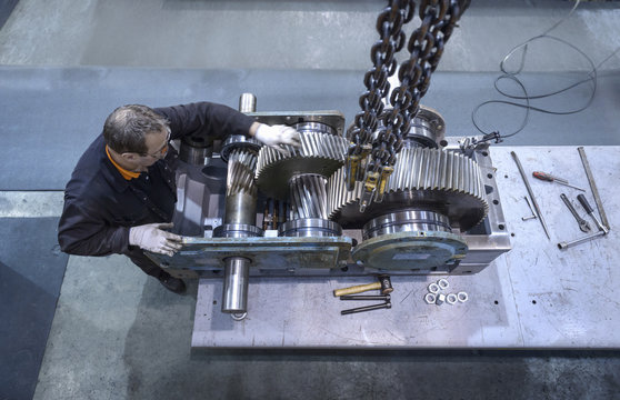 Overhead view of engineer repairing industrial gearbox in factory