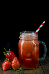 Mason jar con batido o smoothie de fresa y pajita roja espiral sobre mesa de madera vintage y fondo negro