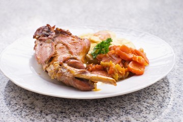 Gourmet roasted rabbit leg with glazed sweet carrot and baked potatoes choped on thin slices. Meal is served on the white simply plate and granit table isolated. Healty and light meal perfect for diet