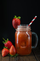 Mason jar con batido o smoothie de fresa y pajita roja espiral sobre mesa de madera vintage y fondo negro